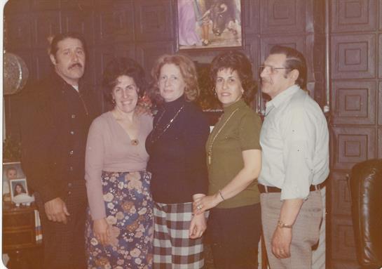 A joyful group of five adults poses warmly in a cozy living room with vintage decor.