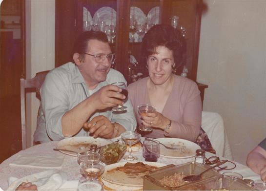 Two people raise glasses in celebration while enjoying a meal at a nicely set dining table.