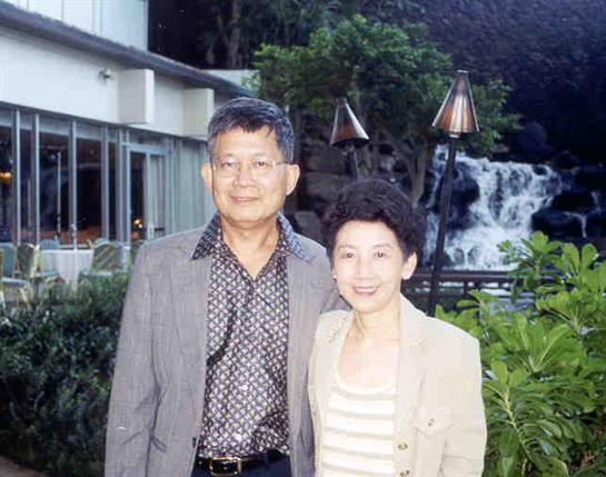 A couple smiles in a lush garden by a waterfall, relishing a peaceful moment.