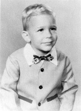A young boy smiles while wearing a button-up outfit with a bow tie, capturing a moment in time.