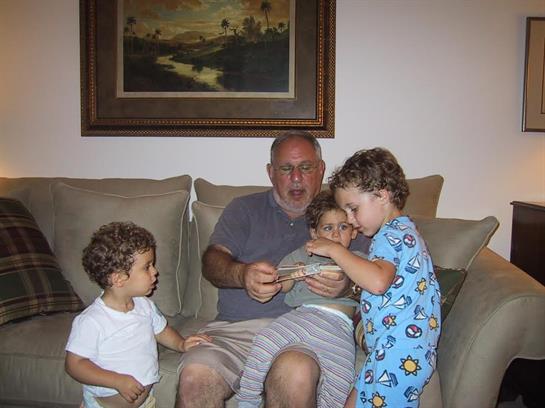Grandfather joyfully interacts with his four young grandchildren while seated on a couch.