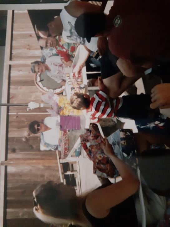 Families gather in a sunny backyard, enjoying food and children playing together happily.