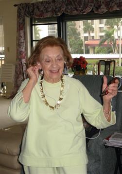 An elderly woman expresses joy while dancing to music in her cozy seaside living room.