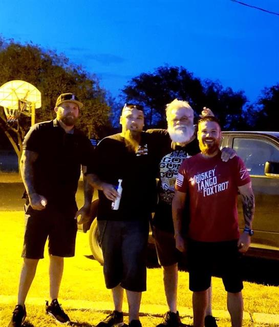 Four friends gather together outdoors, smiling and enjoying each other's company near sunset.