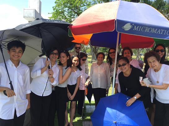People are gathered outdoors, using umbrellas to stay cool during a sunny day in the park.