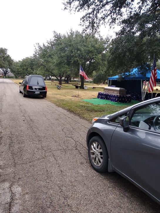 People gather by a memorial with flags and tents on a cloudy day in a park setting.