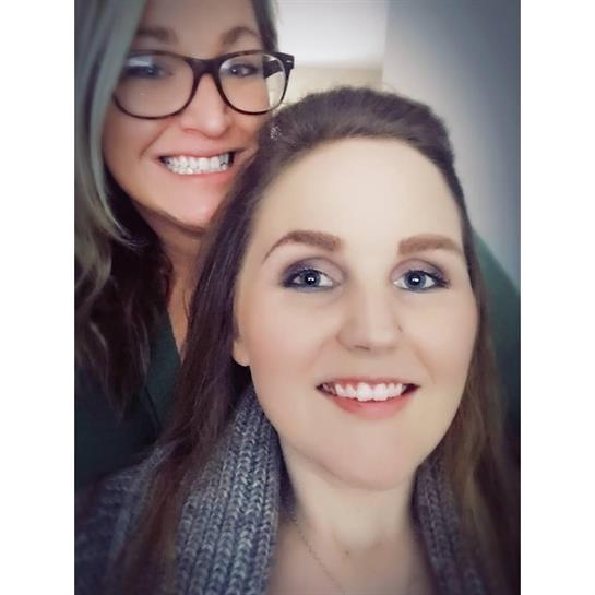 Two friends pose for a selfie, smiling in their casual outfits and natural light.