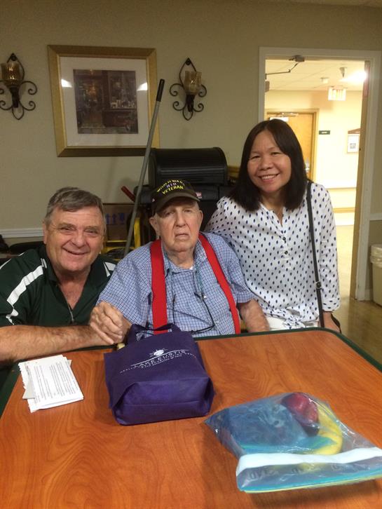 Two visitors smiling with a senior resident at a care facility during afternoon hours.