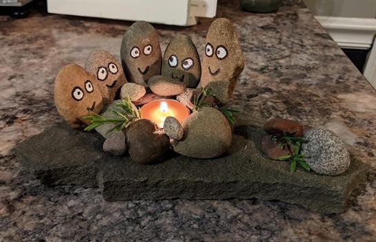 Colorful stone figures with faces sit around a flickering candle, creating a cheerful ambiance.