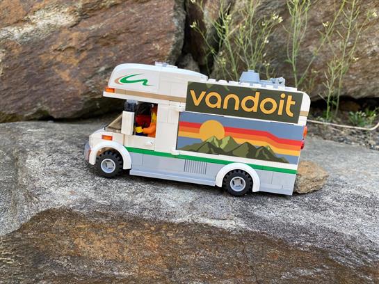 A retro toy camper van stands on rocks, highlighting its colorful design and outdoor spirit.