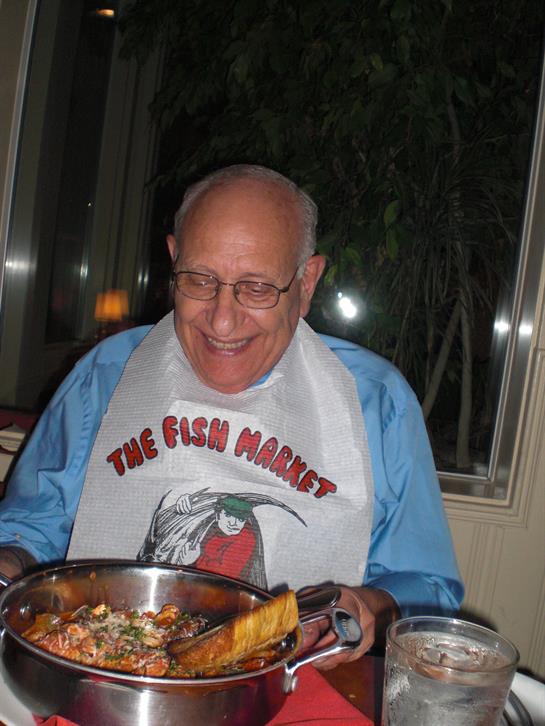 A joyful elderly man is seated at a table in a restaurant savoring a seafood dish.