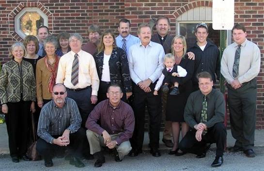 Group of family members and friends smiling and posing outdoors near a brick building.
