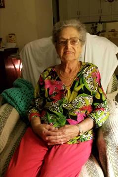 An elderly woman in vibrant clothes relaxes in her serene home.