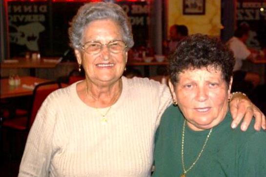 Two joyful women pose together, smiling warmly in a vibrant restaurant setting at night.