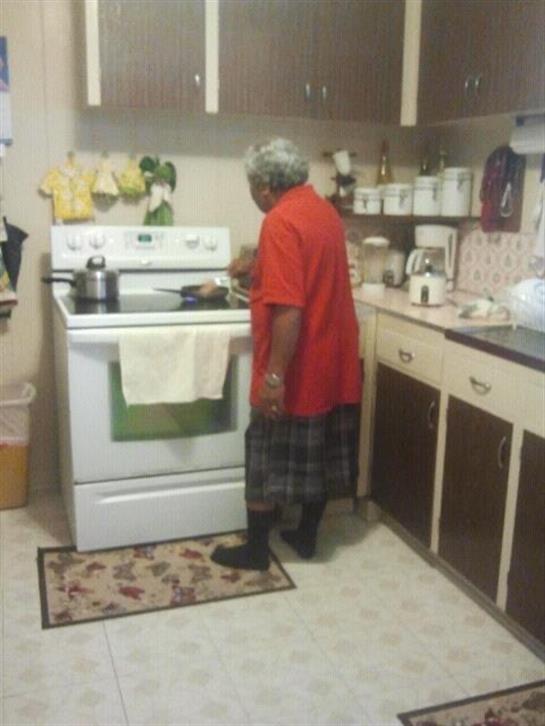 An elderly person stands at the stove in a well-organized kitchen preparing a meal.