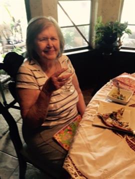 An elderly woman holds up a glass while seated at a table filled with delicious food during lunch.