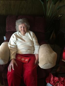 An elderly woman wearing warm clothes sits in a recliner chair, enjoying a quiet moment in her home.
