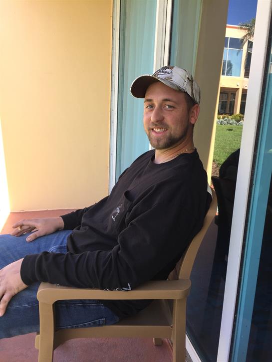 A man relaxes on a balcony, smiling and enjoying the warm sunshine of the day.