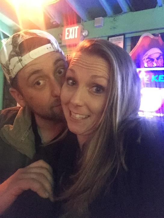 A couple shares a playful moment in a vibrant bar filled with colorful lights and excitement.