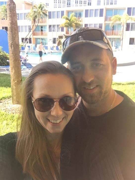 Happy couple smiles while posing outdoors at a resort on a bright sunny day.