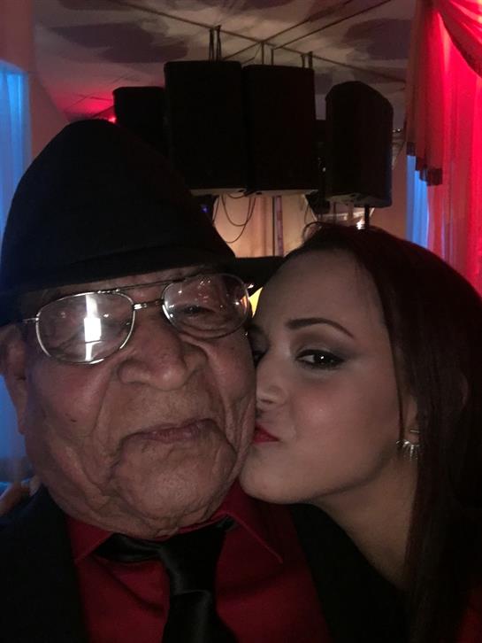 A young woman kisses an elderly man on the cheek, both smiling joyfully at a festive event.