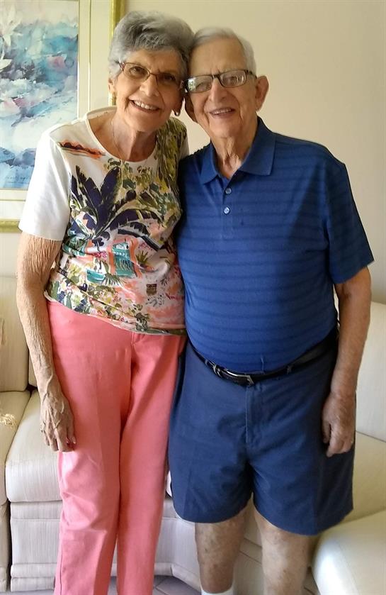 A happy couple stands closely in a well-lit living space, showcasing their affection and bond.