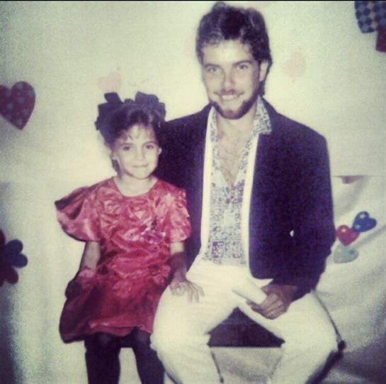 A child in a red dress sits beside an adult in a suit at a festive gathering with heart decorations.