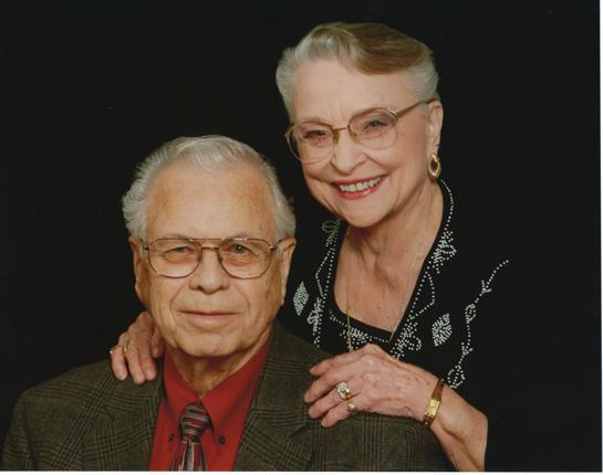 A happy elderly couple stands together, smiling warmly at the camera, embodying love and connection.