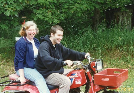A smiling couple takes a joyful ride on a red vehicle surrounded by lush greenery.
