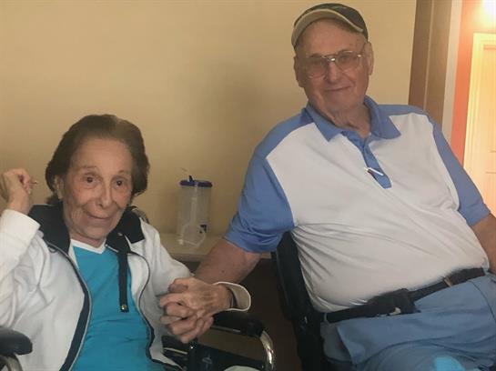 Two elderly people sit hand in hand, smiling and creating a joyful atmosphere.