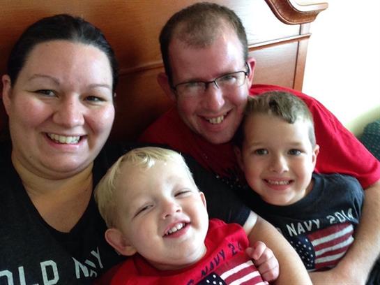 Four family members share a joyful moment, smiling and relaxed in a comfortable bedroom setting.