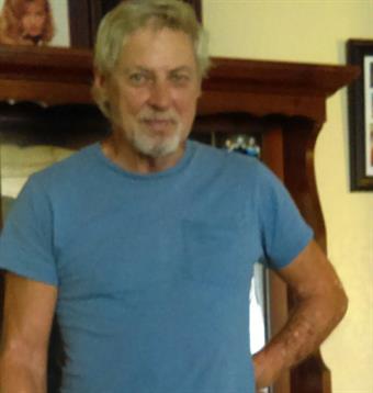 An older man with light hair poses confidently in a warm, inviting living space.