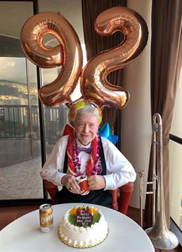 A person happily celebrates their 92nd birthday with balloons and cake.