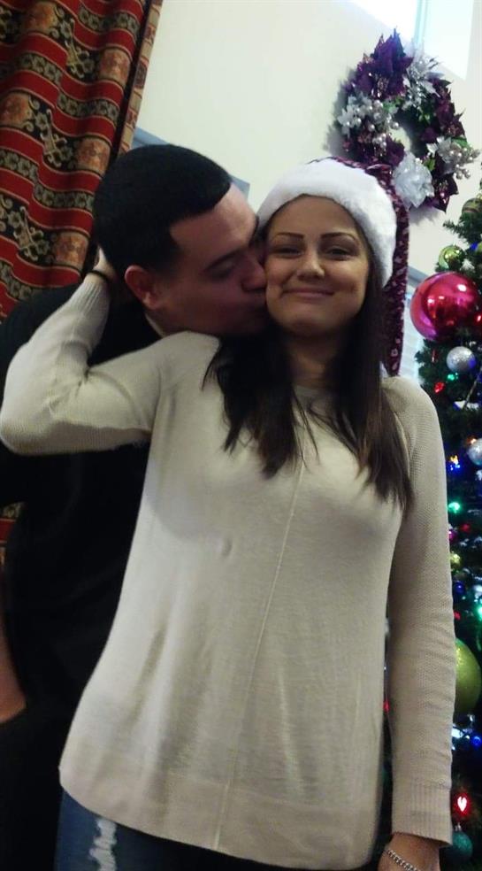 Man kisses woman on the cheek as they smile beside a colorful Christmas tree.