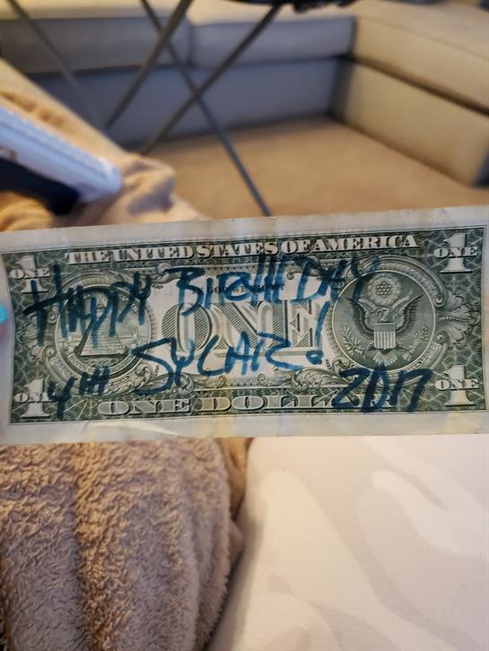 Handwritten birthday wishes on a dollar bill resting on a cozy, soft surface.