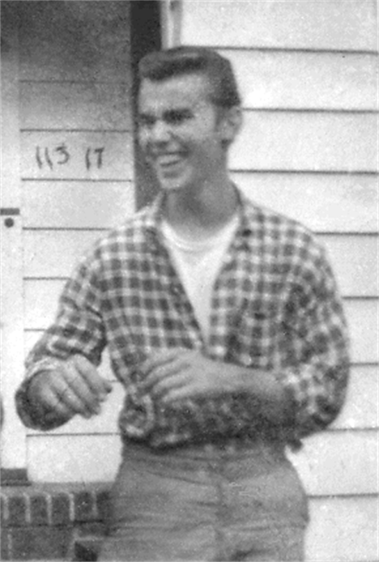A young man enjoys a laugh outside a simple wooden house on a sunny day.
