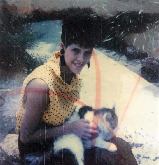 A smiling young woman with a stylish haircut holds a calico cat outdoors on a sunny day.