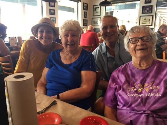 Four cheerful friends sit around a table in a busy restaurant, sharing smiles and laughter.