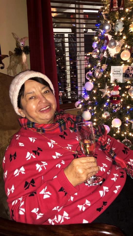 A woman smiles cheerfully while holding a drink next to a beautifully decorated Christmas tree.