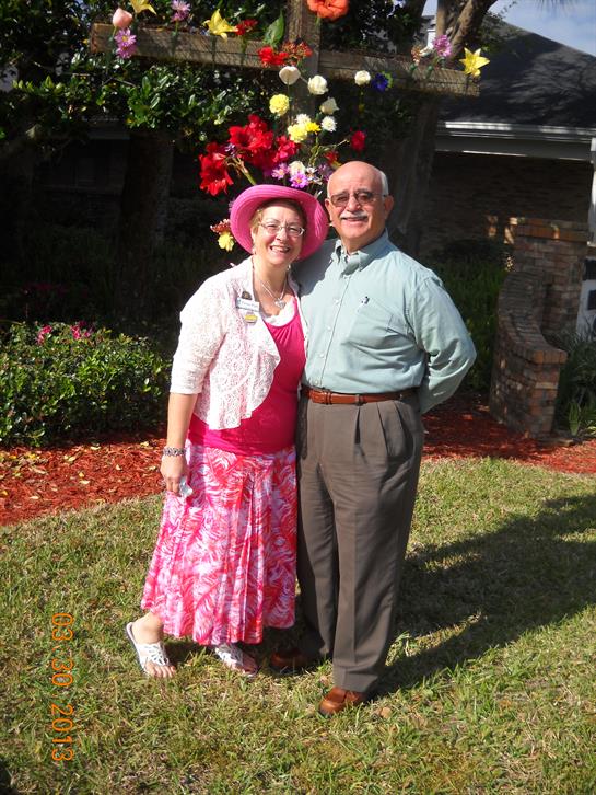 Joyful couple stands together in a vibrant garden adorned with flowers, wearing colorful attire.