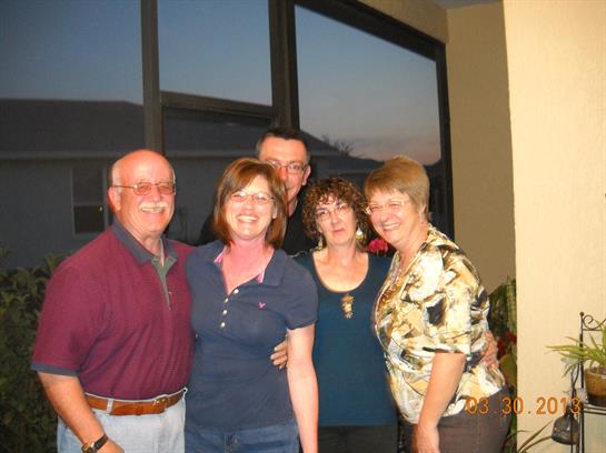 Five friends gather in a warm indoor space, smiling and sharing joyful moments as the sun sets.