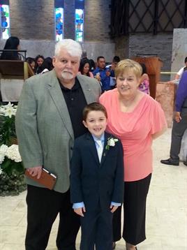 A well-dressed young boy smiles with his grandparents at a family event in an elegant hall.