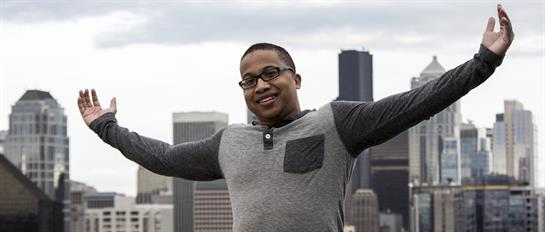 Person smiles broadly with arms outstretched, embracing the urban skyline during daylight.