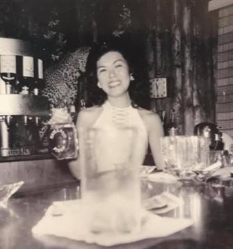A happy woman poses with a drink at a bar, surrounded by elegant glassware and decor.