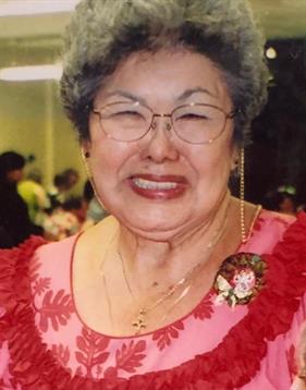 An elderly woman in traditional attire smiles warmly at a cultural event.
