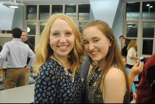 Two young women smile brightly while posing together in a lively social environment.