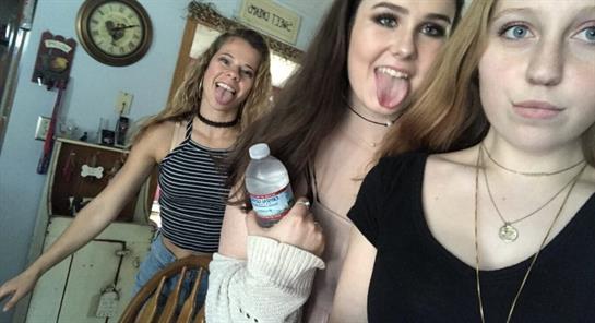 Two friends are playfully posing at home, sticking out their tongues and having fun.