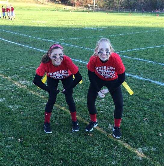 Two enthusiastic players get ready for a flag football match on a grassy field at sunset.