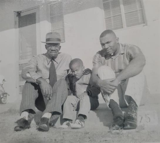 Three family members relax on the steps of their house, enjoying time together in the sun.