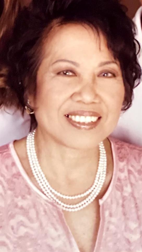 Smiling woman exudes joy, adorned in pearls, brightening the atmosphere with her presence.